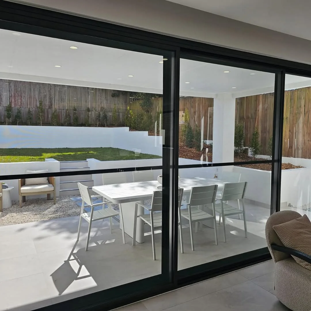 Black framed aluminium sliding doors opening onto a covered alfresco dining area - AGM Windows & Doors, Sydney